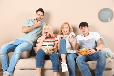 Young friends with snacks watching TV on sofa at home