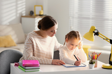 Photo of Woman helping her daughter with homework at table indoors