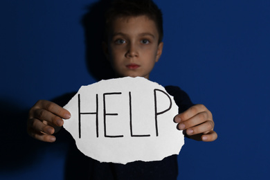 Abused little boy with sign HELP near blue wall, focus on hands. Domestic violence concept