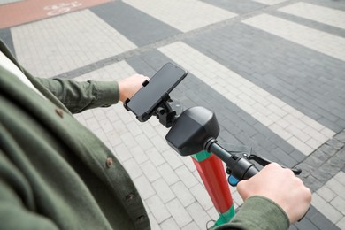Photo of Man riding electric kick scooter with smartphone outdoors, closeup