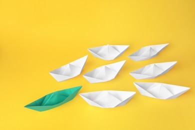 Photo of Group of paper boats following green one on yellow background. Leadership concept