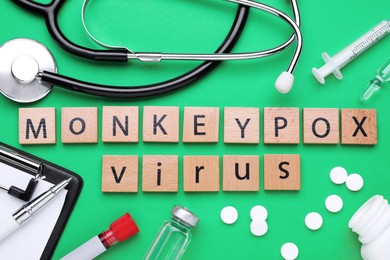 Flat lay composition with words Monkeypox Virus made of wooden squares and medical supplies on green background