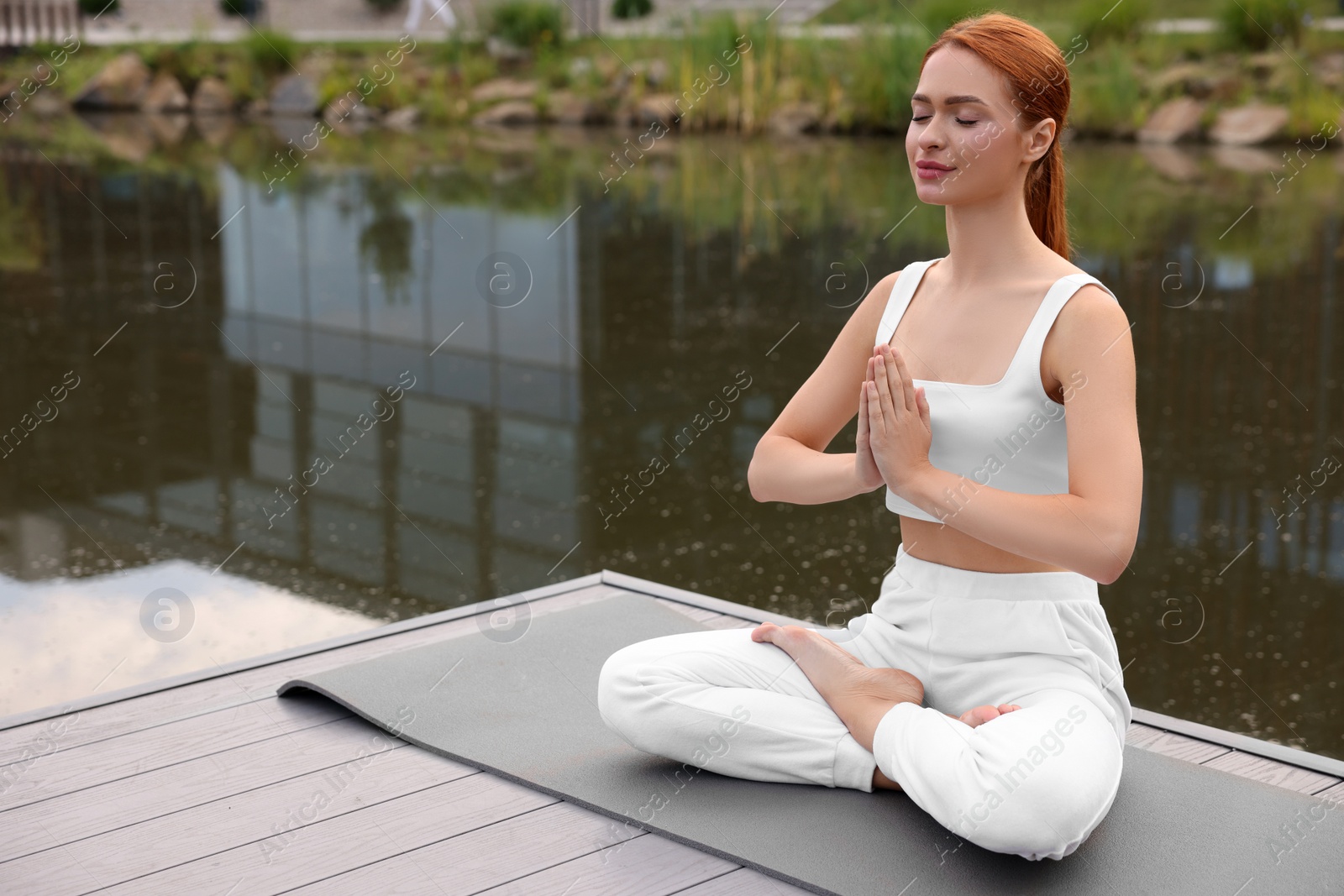 Photo of Beautiful young woman practicing Padmasana on yoga mat outdoors, space for text. Lotus pose