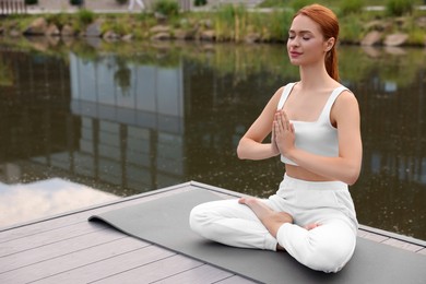 Beautiful young woman practicing Padmasana on yoga mat outdoors, space for text. Lotus pose