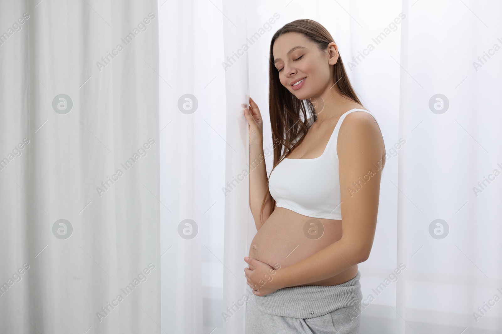 Photo of Beautiful pregnant woman near window indoors, space for text