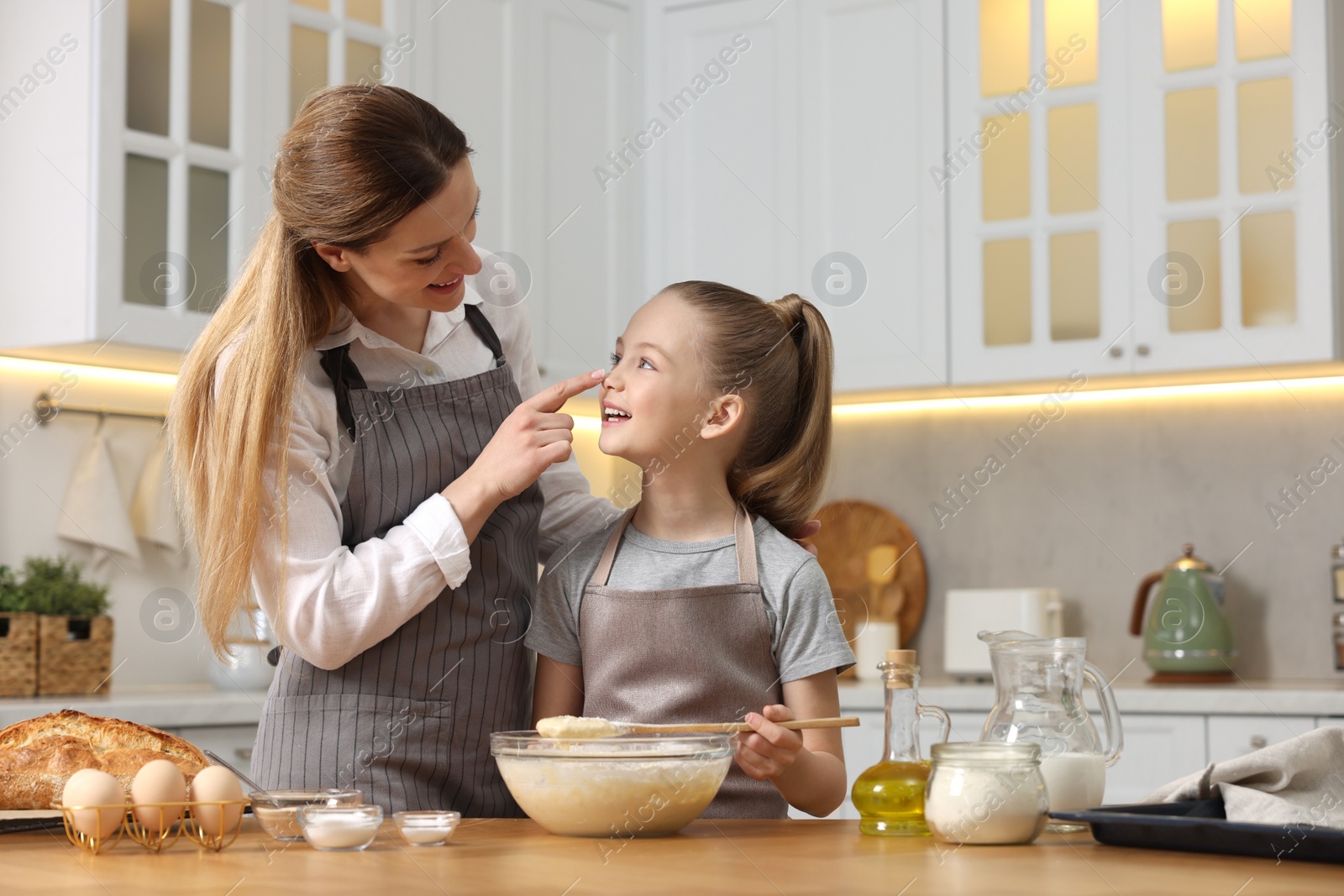 Photo of Making bread. Mother and her daughter preparing dough in bowl at wooden table in kitchen