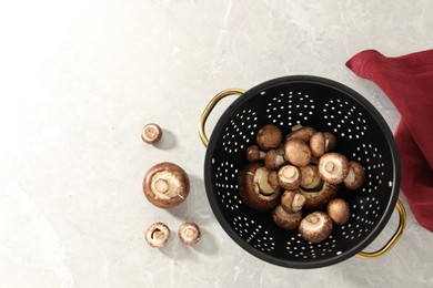 Photo of Raw mushrooms in black colander on marble table, flat lay. Space for text