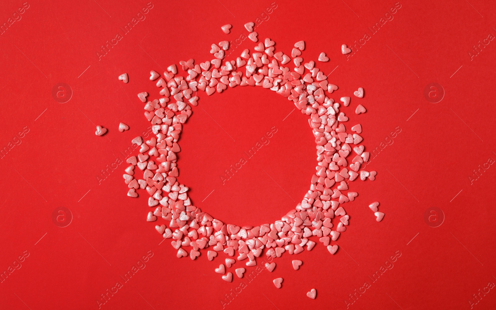 Photo of Round frame made of bright heart shaped sprinkles on red background, flat lay. Space for text