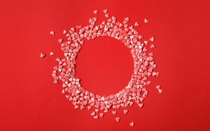Round frame made of bright heart shaped sprinkles on red background, flat lay. Space for text