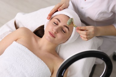 Photo of Cosmetologist making face massage with roller to client in clinic, top view
