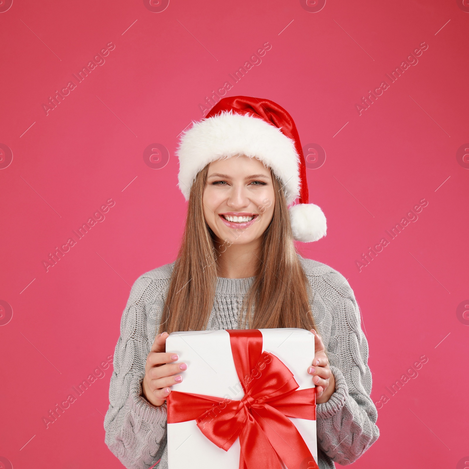 Photo of Happy young woman in Santa hat with Christmas gift on pink background