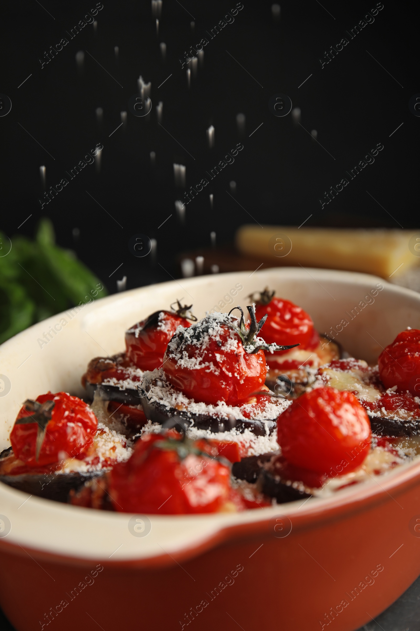 Photo of Grating cheese onto baked eggplant with tomatoes, closeup