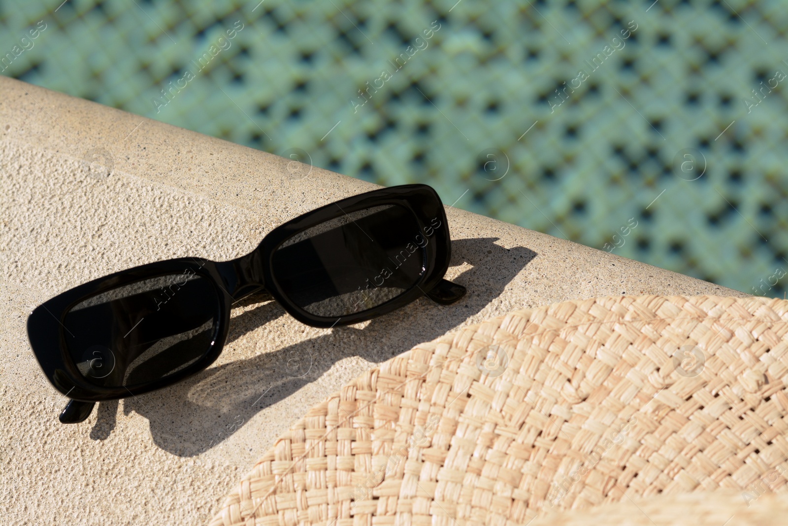 Photo of Stylish sunglasses near outdoor swimming pool on sunny day, closeup