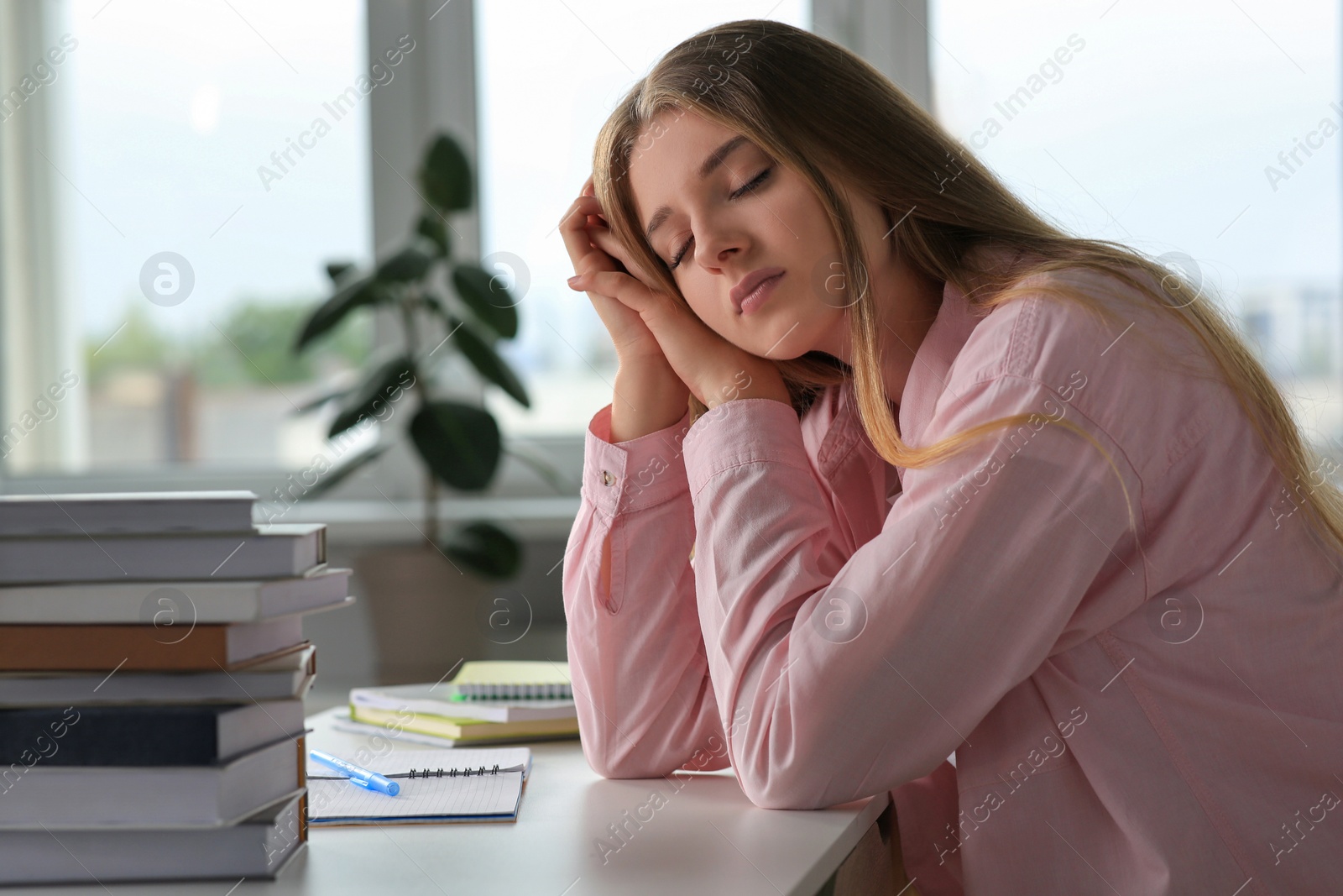 Photo of Young tired woman sleeping near books at white table indoors