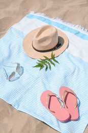 Photo of Beach towel with straw hat, sunglasses, leaves and flip flops on sand