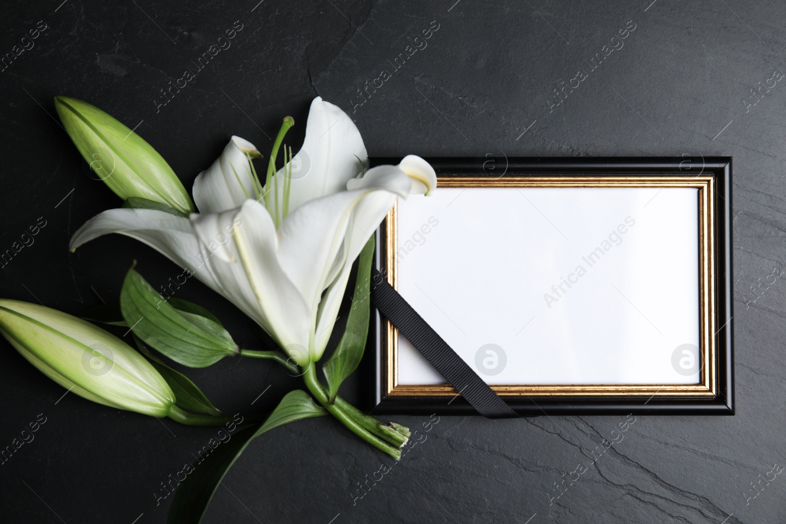 Photo of Funeral photo frame with ribbon and white lily on black table, flat lay. Space for design