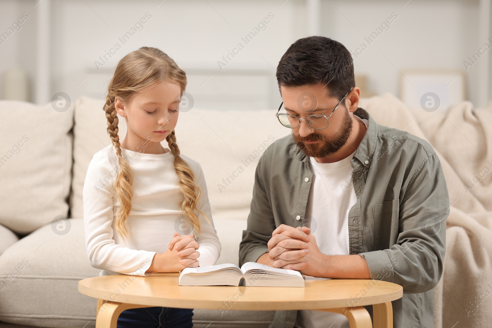 Photo of Girl and her godparent praying over Bible together at table indoors