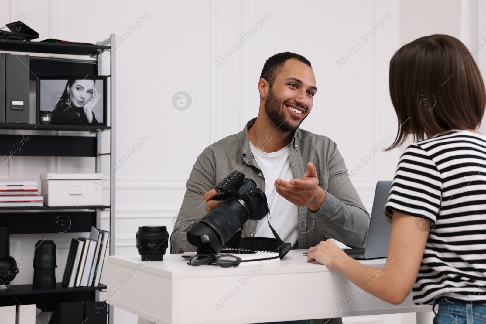 Photo of Young professional photographer holding camera while talking with woman in modern photo studio