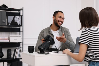 Young professional photographer holding camera while talking with woman in modern photo studio