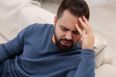 Unhappy man suffering from headache on sofa indoors