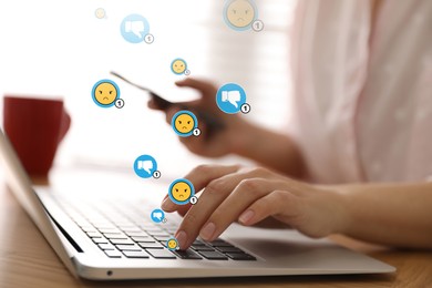 Image of Social media dislike reaction. Woman using laptop and mobile phone at table, closeup. Thumbs down and angry face emoji illustrations over device