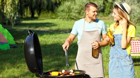 Happy couple cooking food on barbecue grill in park