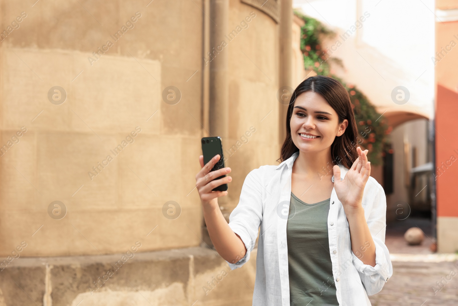 Photo of Beautiful young woman using smartphone near building outdoors