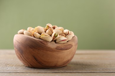 Tasty pistachios in bowl on wooden table against olive background, closeup. Space for text