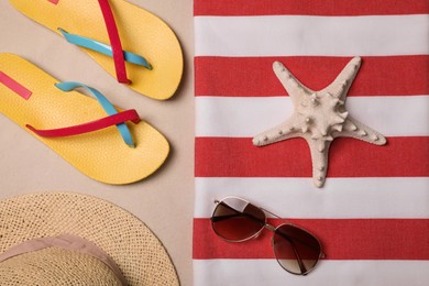 Photo of Beach towel, hat, sunglasses, starfish and flip flops on sand, flat lay