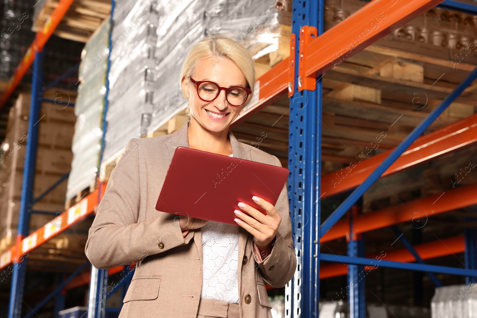 Photo of Happy manager using modern tablet in warehouse with lots of products