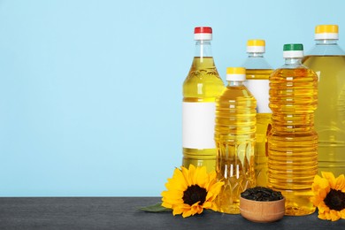 Bottles of cooking oil, sunflowers and seeds on wooden table, space for text