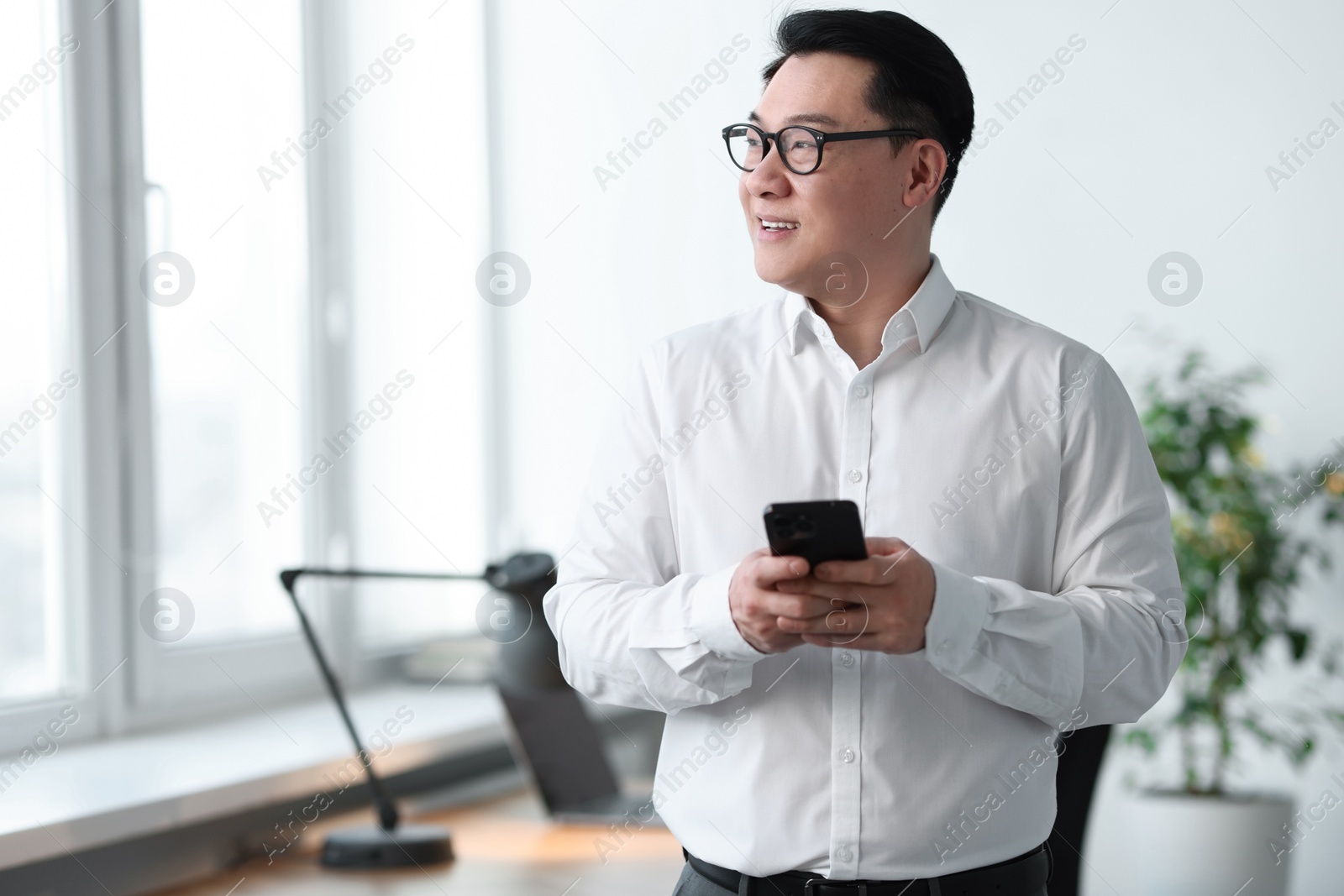 Photo of Portrait of smiling businessman with smartphone in office. Space for text