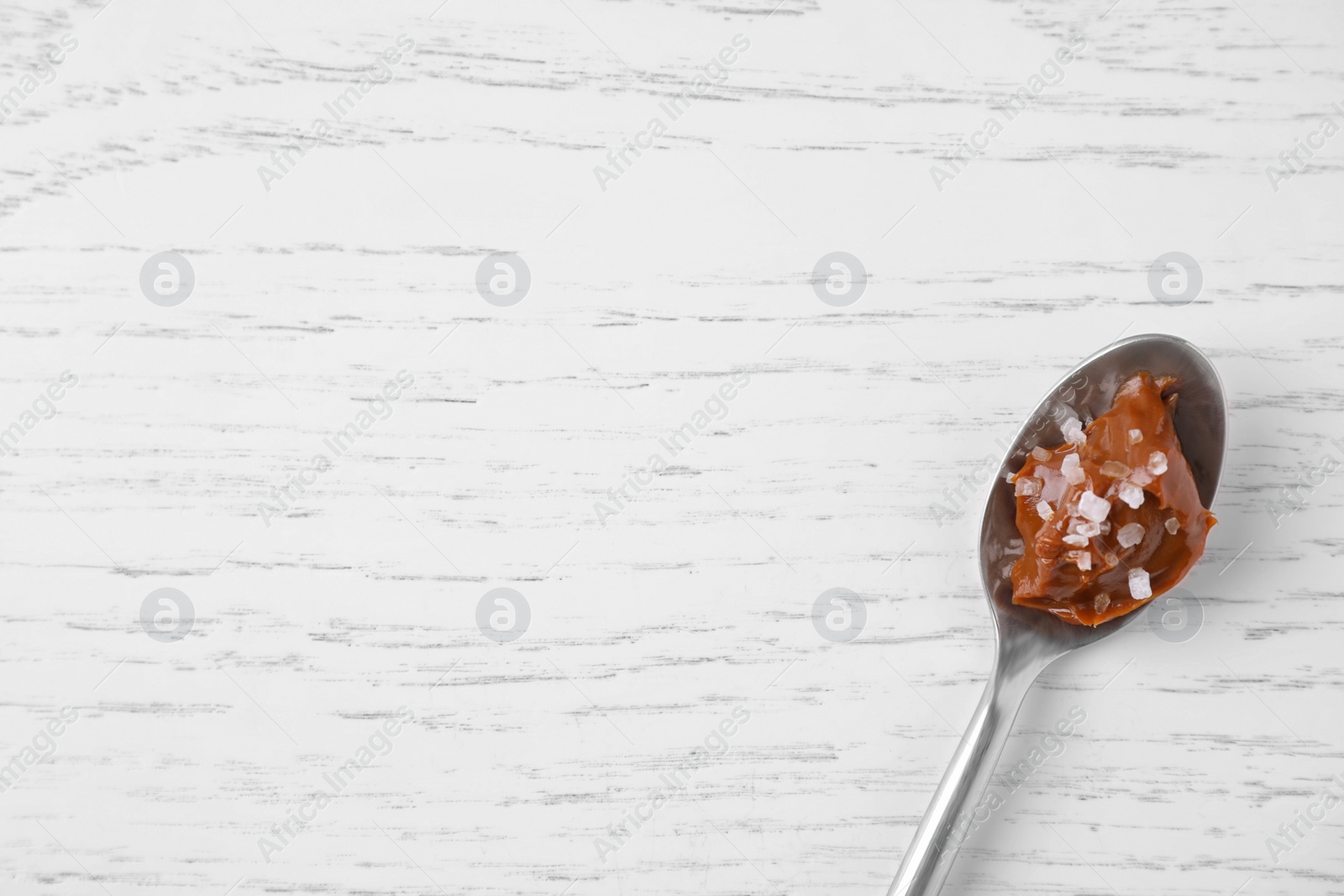 Photo of Delicious salted caramel on white wooden table, top view. Space for text