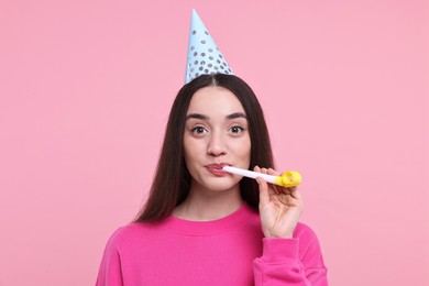 Woman in party hat with blower on pink background