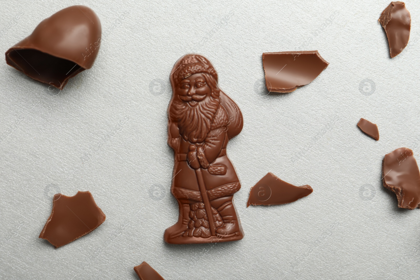 Photo of Flat lay composition with whole and broken chocolate Santa Claus candies on light grey table