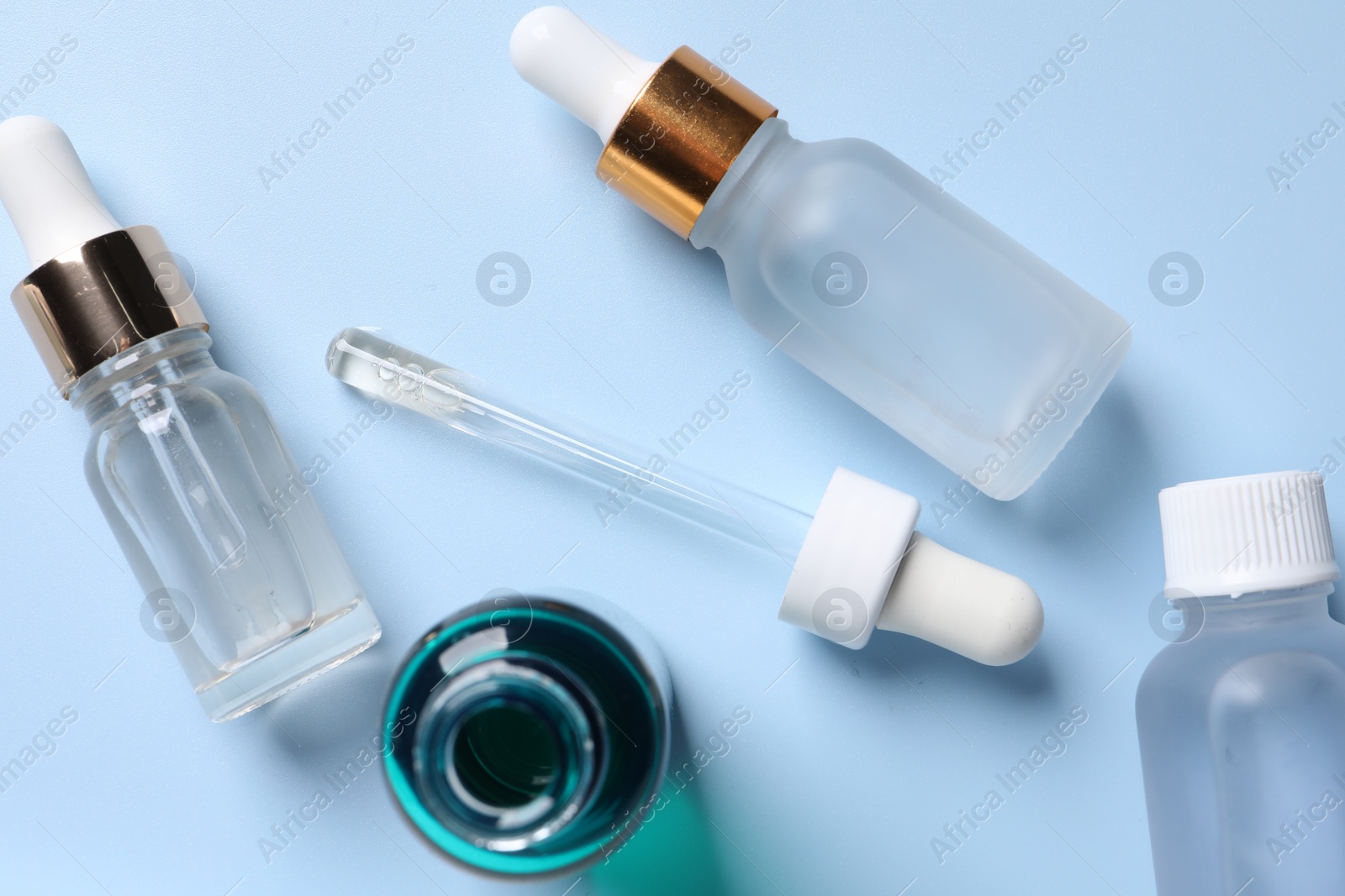 Photo of Bottles of cosmetic serum on light blue background, flat lay