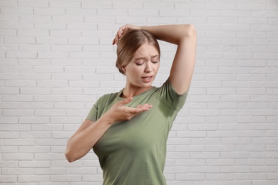 Young woman with sweat stain on her clothes against brick wall. Using deodorant