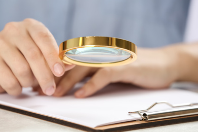 Woman using magnifying glass at table, closeup