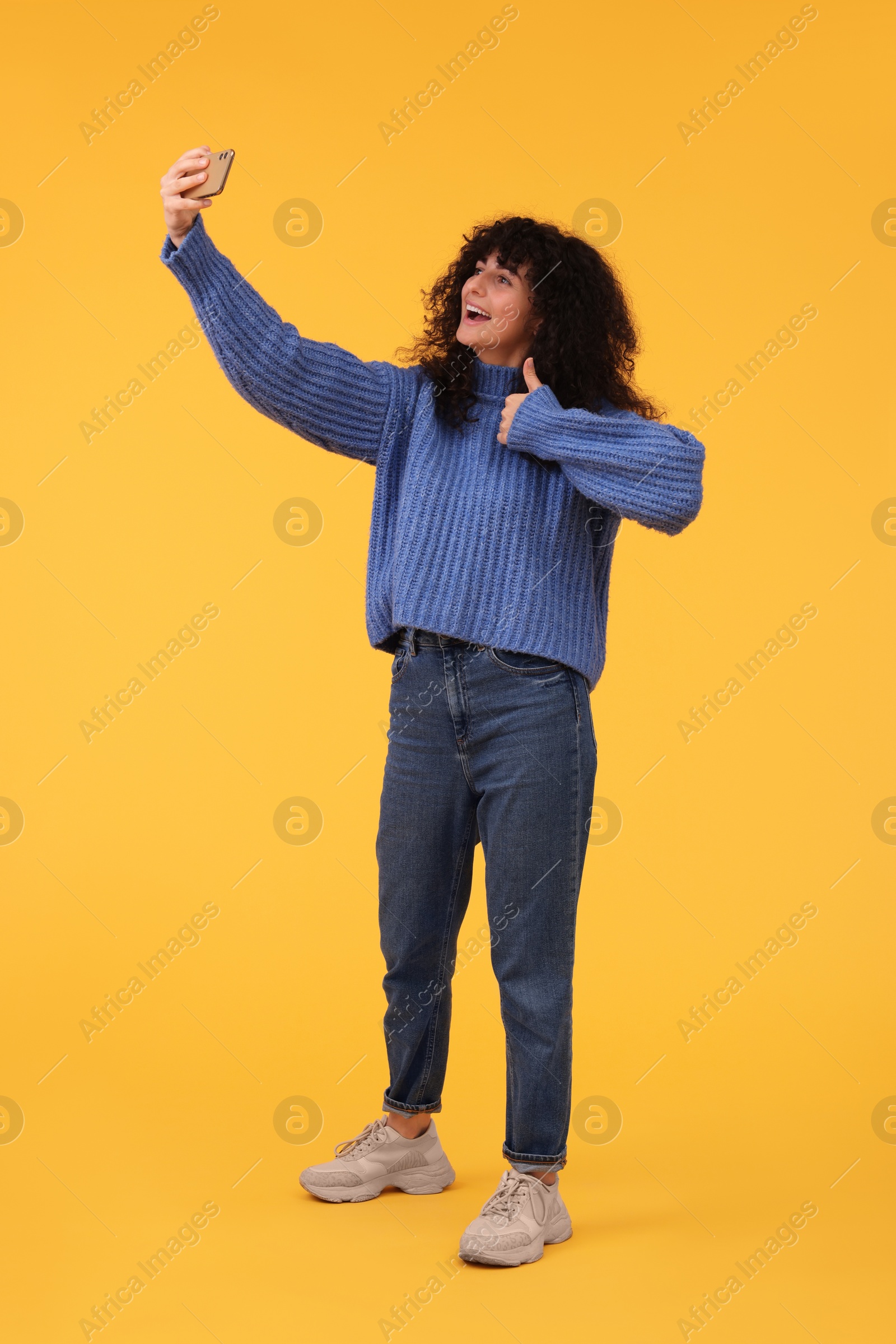 Photo of Beautiful young woman taking selfie with smartphone on orange background