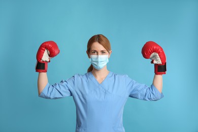 Photo of Doctor with protective mask and boxing gloves on light blue background. Strong immunity concept