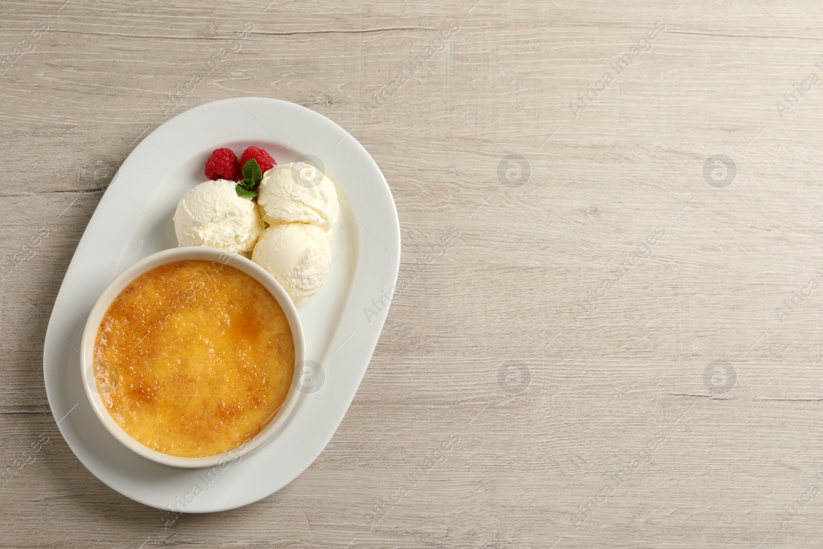 Photo of Delicious creme brulee with scoops of ice cream, fresh raspberries and mint on light wooden table, top view. Space for text