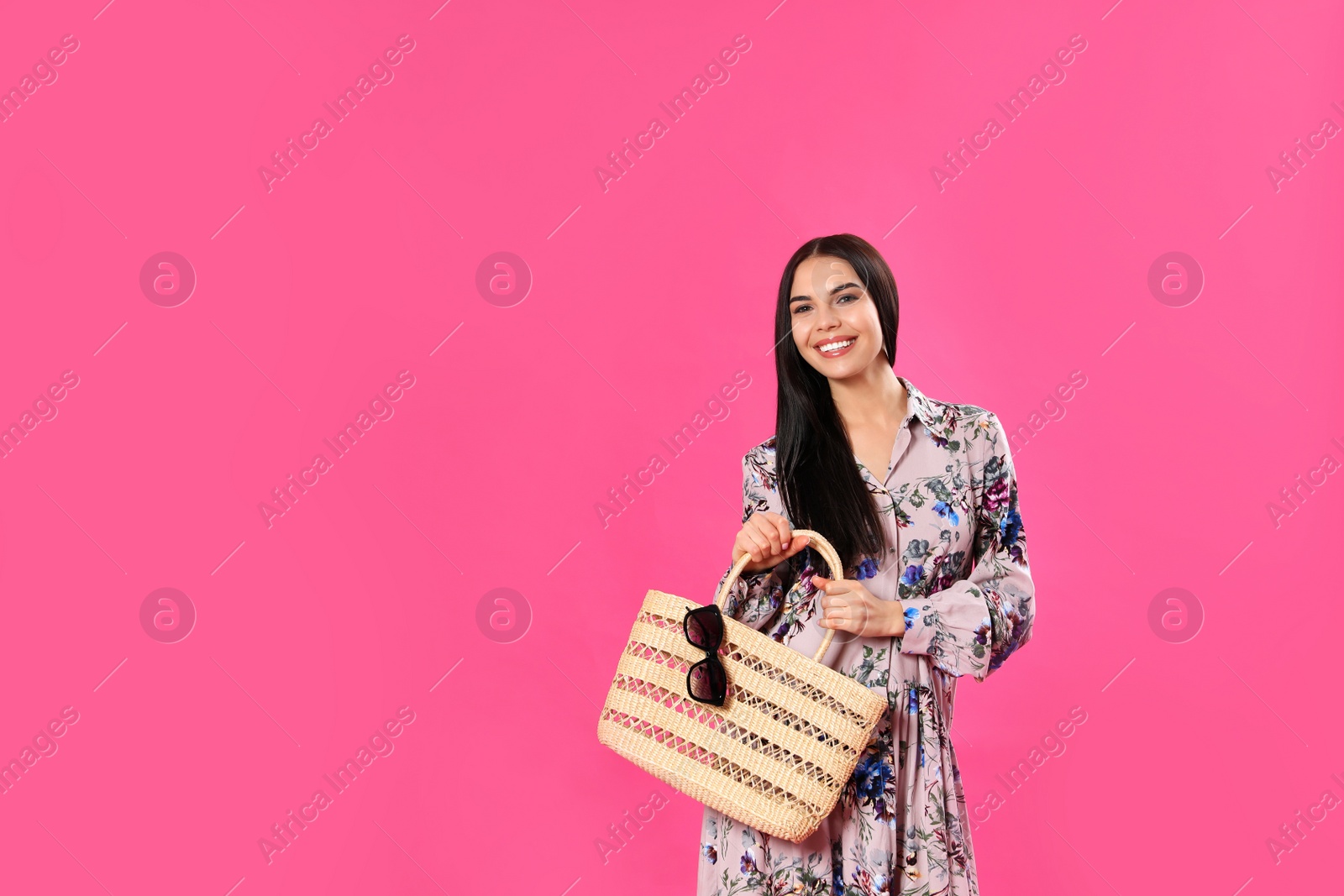 Photo of Young woman wearing floral print dress with straw bag on pink background. Space for text
