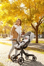 Photo of Happy mother with her baby daughter in stroller outdoors on autumn day