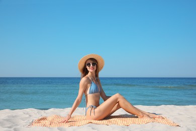 Photo of Beautiful woman sitting on beach towel near sea