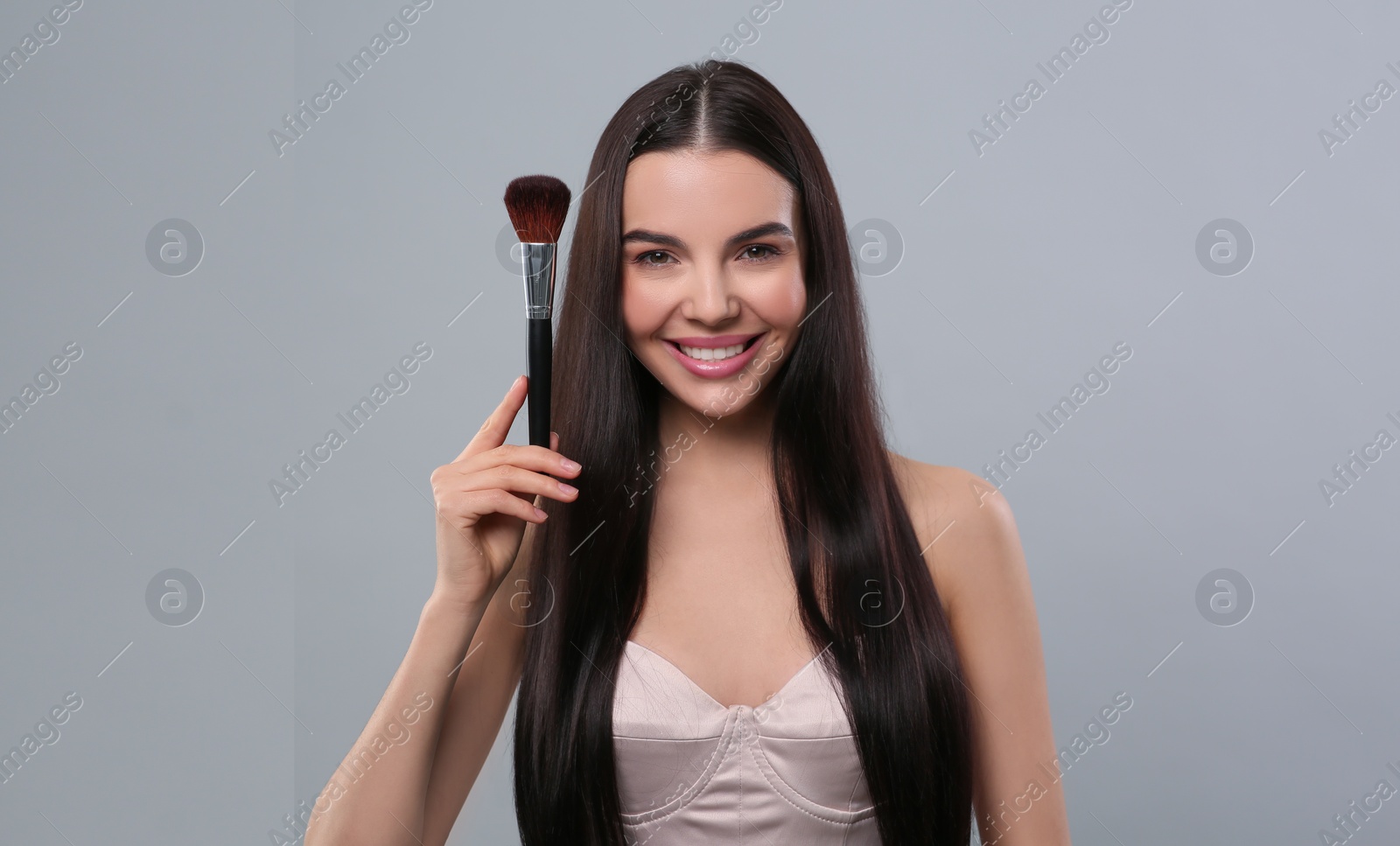 Photo of Happy woman with makeup brush on light grey background