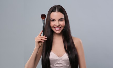 Happy woman with makeup brush on light grey background