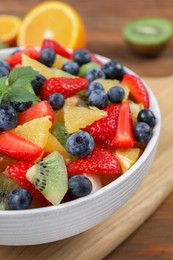 Photo of Delicious fresh fruit salad in bowl on wooden table, closeup