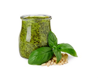 Tasty pesto sauce in glass jar, pine nuts and basil on white background