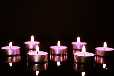 Image of Beautiful burning violet candles on black background. Funeral attributes