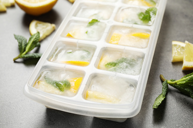 Photo of Ice cubes with lemon and mint in tray on grey table, closeup